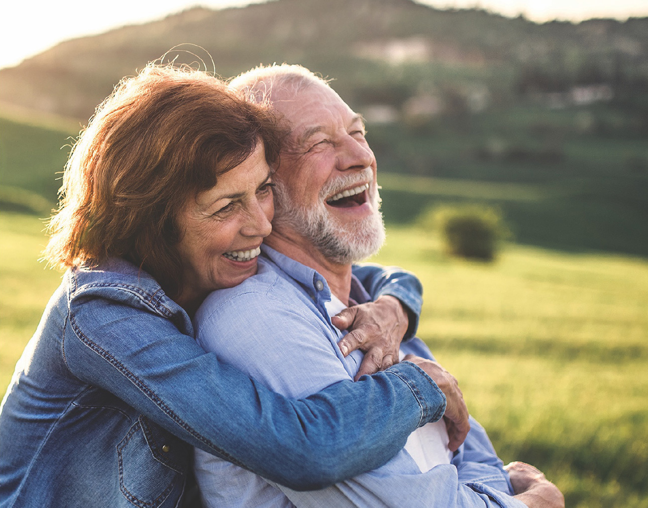 Smiling couple embacing in a field at sunset.